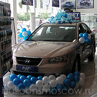 Новый автомобиль в автосалоне украшен голубыми и белыми воздушными шарами
